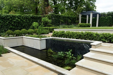 Photo of a large transitional backyard formal garden in London with with pond and natural stone pavers.