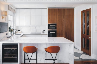 Photo of a mid-sized contemporary u-shaped open plan kitchen in London with a double-bowl sink, flat-panel cabinets, white cabinets, marble benchtops, white splashback, marble splashback, black appliances, marble floors, a peninsula, multi-coloured floor and white benchtop.