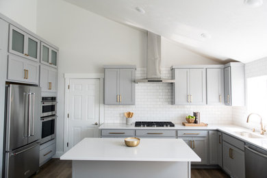 Example of a mid-sized beach style l-shaped laminate floor and brown floor eat-in kitchen design in Salt Lake City with shaker cabinets, quartz countertops, white backsplash, an island, white countertops, an undermount sink, blue cabinets, ceramic backsplash and stainless steel appliances