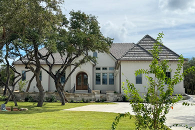 Inspiration for a large french country white one-story stucco house exterior remodel in Austin with a tile roof and a brown roof
