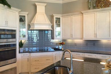 Mid-sized farmhouse l-shaped light wood floor and beige floor eat-in kitchen photo in Miami with an undermount sink, shaker cabinets, white cabinets, granite countertops, blue backsplash, glass tile backsplash, stainless steel appliances and an island