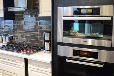 Large trendy galley dark wood floor enclosed kitchen photo in Calgary with an undermount sink, shaker cabinets, white cabinets, quartzite countertops, multicolored backsplash, glass tile backsplash, stainless steel appliances and an island