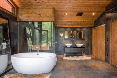 This is an example of a contemporary master bathroom in New York with a freestanding tub, gray tile, stone tile, grey walls, slate floors, a vessel sink, a corner shower, brown floor and a hinged shower door.