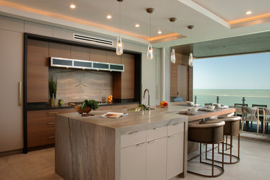 Example of a trendy galley gray floor and tray ceiling kitchen design in Other with an undermount sink, flat-panel cabinets, medium tone wood cabinets, gray backsplash, stone slab backsplash, an island and gray countertops