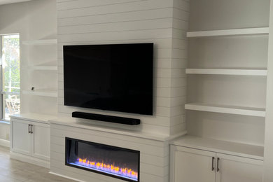 Photo of a large family room in Tampa with grey walls, ceramic floors, a standard fireplace, a wall-mounted tv, grey floor and planked wall panelling.