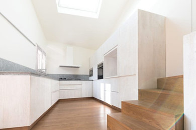 Immagine di una cucina design di medie dimensioni con lavello integrato, ante a filo, ante bianche, top in pietra calcarea, paraspruzzi grigio, paraspruzzi in pietra calcarea, elettrodomestici neri, pavimento in legno massello medio, nessuna isola, pavimento marrone e top grigio