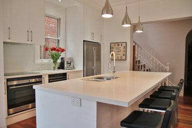 Mid-sized contemporary galley eat-in kitchen in Melbourne with an undermount sink, flat-panel cabinets, white cabinets, quartz benchtops, white splashback, glass sheet splashback, stainless steel appliances, medium hardwood floors and with island.