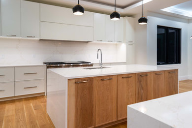 Example of a transitional light wood floor and tray ceiling kitchen design in Boston with an undermount sink, shaker cabinets, quartz countertops, quartz backsplash, stainless steel appliances and two islands