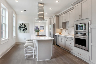 Example of a large trendy single-wall medium tone wood floor enclosed kitchen design in Houston with an undermount sink, shaker cabinets, gray cabinets, quartzite countertops, gray backsplash, marble backsplash, stainless steel appliances and an island
