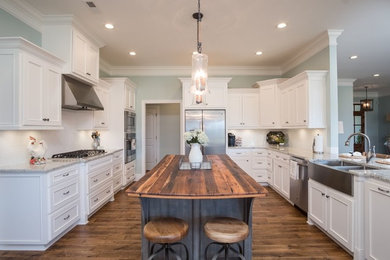 Country kitchen in Birmingham with a farmhouse sink, recessed-panel cabinets, white cabinets, wood benchtops, white splashback, stainless steel appliances, dark hardwood floors, with island and brown floor.