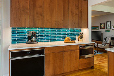 Example of a mid-sized trendy l-shaped medium tone wood floor eat-in kitchen design in Detroit with an undermount sink, flat-panel cabinets, medium tone wood cabinets, quartz countertops, green backsplash, ceramic backsplash, stainless steel appliances, a peninsula and white countertops