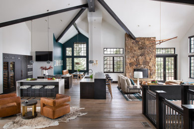 Example of a huge mountain style open concept medium tone wood floor, brown floor and vaulted ceiling living room design in Denver with white walls, a standard fireplace, a stacked stone fireplace and a wall-mounted tv