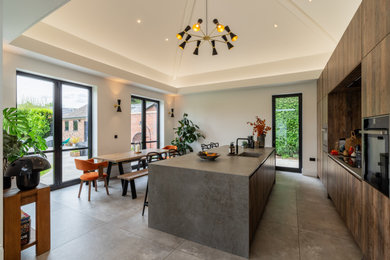 Photo of a large contemporary kitchen/diner in Cheshire with flat-panel cabinets, distressed cabinets, concrete worktops, grey splashback, porcelain flooring, an island, grey floors, grey worktops and a vaulted ceiling.