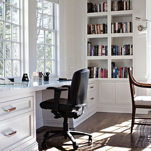 Expansive country home office in New York with a library, white walls, dark hardwood floors, no fireplace, a built-in desk and brown floor.