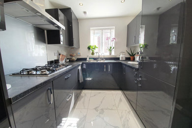 Photo of a medium sized contemporary kitchen/diner in Essex with a double-bowl sink, flat-panel cabinets, grey cabinets, laminate countertops, grey splashback, glass sheet splashback, stainless steel appliances, ceramic flooring, no island and grey worktops.