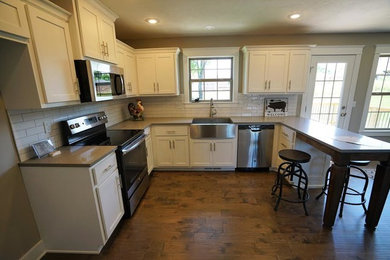 Bild på ett stort vintage kök, med en rustik diskho, skåp i shakerstil, vita skåp, bänkskiva i kvartsit, vitt stänkskydd, stänkskydd i tunnelbanekakel, rostfria vitvaror, mellanmörkt trägolv, en halv köksö och brunt golv