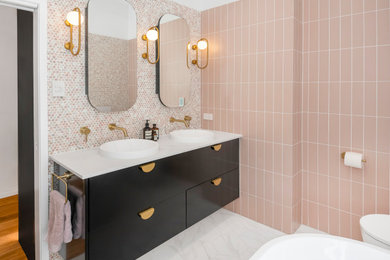 This is an example of a large contemporary master bathroom in Brisbane with furniture-like cabinets, black cabinets, a freestanding tub, an open shower, a wall-mount toilet, pink tile, mosaic tile, pink walls, ceramic floors, a vessel sink, marble benchtops, black floor, an open shower, white benchtops, a niche, a double vanity and a floating vanity.