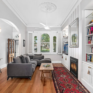 Inspiration for a victorian open concept family room in Sydney with white walls, medium hardwood floors, a standard fireplace, a built-in media wall and brown floor.