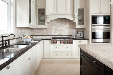 Large transitional l-shaped kitchen in Other with a double-bowl sink, recessed-panel cabinets, white cabinets, beige splashback, stainless steel appliances, with island and stone tile splashback.