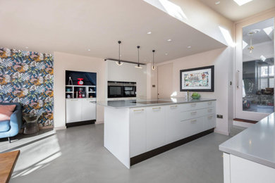Photo of a large modern grey and white open plan kitchen in Other with a single-bowl sink, flat-panel cabinets, white cabinets, quartz worktops, grey splashback, stone slab splashback, black appliances, concrete flooring, an island, grey floors, grey worktops and a feature wall.