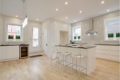 Inspiration for a mid-sized contemporary light wood floor kitchen remodel in Montreal with a single-bowl sink, white cabinets, gray backsplash, stone tile backsplash and an island