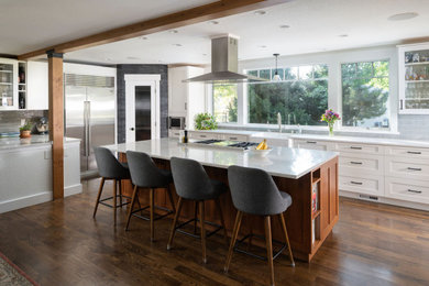 Mid-sized transitional galley medium tone wood floor, brown floor and exposed beam eat-in kitchen photo in Denver with a farmhouse sink, shaker cabinets, white cabinets, quartz countertops, gray backsplash, ceramic backsplash, stainless steel appliances, an island and white countertops