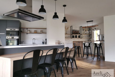 This is an example of a large industrial kitchen/diner in Nantes with a submerged sink, grey cabinets, white splashback, integrated appliances, medium hardwood flooring and multiple islands.