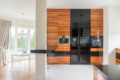 This is an example of a large midcentury eat-in kitchen in Los Angeles with flat-panel cabinets, medium wood cabinets, black appliances, marble floors, a peninsula, beige floor, a drop-in sink and white splashback.