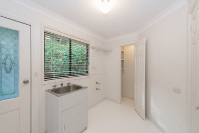 Inspiration for a mid-sized traditional galley laundry cupboard in Sydney with a single-bowl sink, white walls, ceramic floors and white floor.