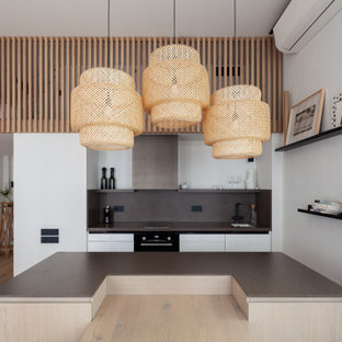 На фото: кухни-гостиные в скандинавском стиле с одинарной раковиной, плоскими фасадами, белыми фасадами, серым фартуком, светлым паркетным полом, островом, бежевым полом и серой столешницей