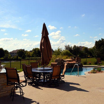 Free form pool with stone table, sun shelf, water feature, and outdoor kitchen,