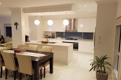 Photo of a large contemporary galley eat-in kitchen in Sydney with a double-bowl sink, white cabinets, quartz benchtops, white splashback, window splashback, stainless steel appliances, ceramic floors, with island, white floor, white benchtop and flat-panel cabinets.