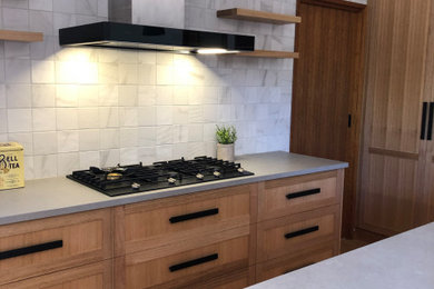 Inspiration for a mid-sized contemporary u-shaped kitchen in Other with a double-bowl sink, shaker cabinets, medium wood cabinets, concrete benchtops, grey splashback, marble splashback, black appliances, light hardwood floors, with island, brown floor and grey benchtop.