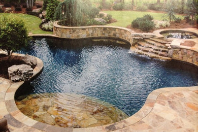 Photo of a large tropical backyard custom-shaped pool in Orange County with a water feature and stamped concrete.