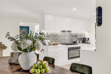 Design ideas for a large contemporary single-wall eat-in kitchen in Sunshine Coast with flat-panel cabinets, white cabinets, quartz benchtops, multi-coloured splashback, glass sheet splashback, vinyl floors and white benchtop.