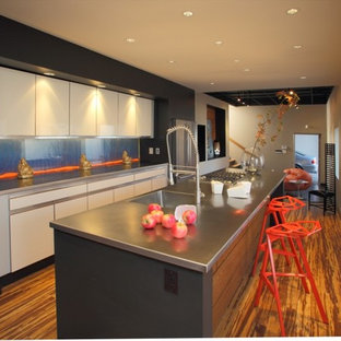 Diseño de cocina de galera, moderna, cerrada, con electrodomésticos de acero inoxidable, fregadero integrado, armarios con paneles lisos, puertas de armario beige, encimera de acero inoxidable y salpicadero de vidrio templado