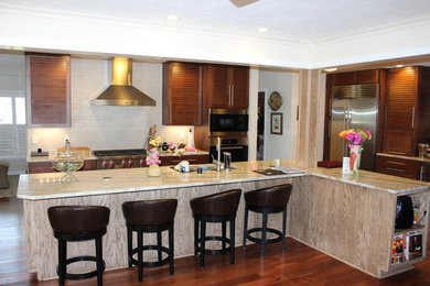 Example of a mid-sized transitional l-shaped medium tone wood floor eat-in kitchen design in Orlando with an undermount sink, louvered cabinets, brown cabinets, granite countertops, white backsplash, glass tile backsplash, stainless steel appliances and an island