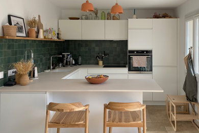 Exemple d'une cuisine ouverte tendance en U de taille moyenne avec un évier 1 bac, des portes de placard blanches, une crédence verte, un sol en travertin et un sol beige.