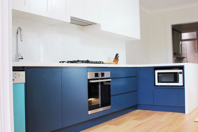 Mid-sized modern l-shaped kitchen in Sydney with flat-panel cabinets, blue cabinets, quartz benchtops, white splashback, light hardwood floors, no island and white benchtop.