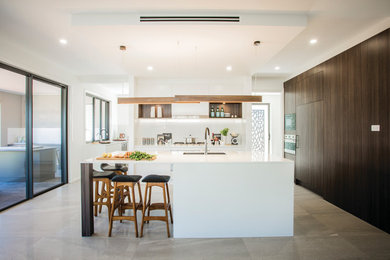 This is an example of a large contemporary galley open plan kitchen in Sydney with dark wood cabinets, quartz benchtops, white splashback, glass sheet splashback, stainless steel appliances, ceramic floors, with island, an undermount sink and grey floor.