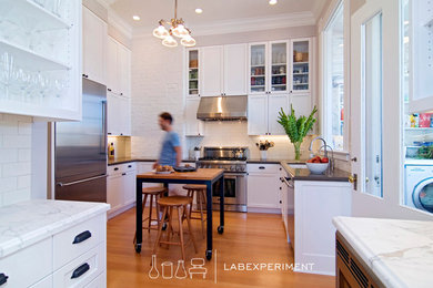 Enclosed kitchen - mid-sized transitional u-shaped medium tone wood floor enclosed kitchen idea in San Francisco with an undermount sink, recessed-panel cabinets, white cabinets, solid surface countertops, white backsplash, subway tile backsplash, stainless steel appliances and an island