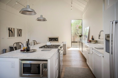 Large trendy single-wall light wood floor open concept kitchen photo in San Francisco with a farmhouse sink, shaker cabinets, white cabinets, marble countertops, stainless steel appliances and an island