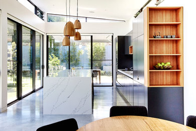 Inspiration for a large contemporary single-wall eat-in kitchen in Sydney with an undermount sink, black cabinets, concrete floors, with island, white splashback, black appliances, quartz benchtops, stone slab splashback, grey floor and white benchtop.