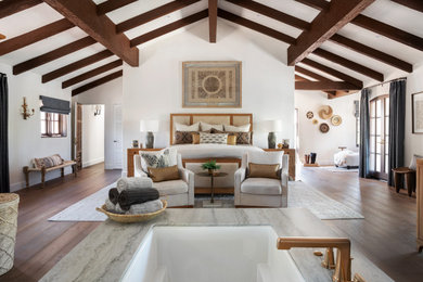 Inspiration for a large mediterranean loft-style medium tone wood floor and exposed beam bedroom remodel in Orange County with white walls