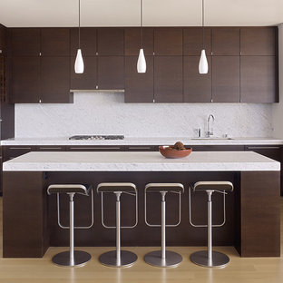 Modelo de cocina minimalista con electrodomésticos de acero inoxidable, armarios con paneles lisos, puertas de armario de madera en tonos medios, salpicadero blanco, salpicadero de losas de piedra y fregadero bajoencimera