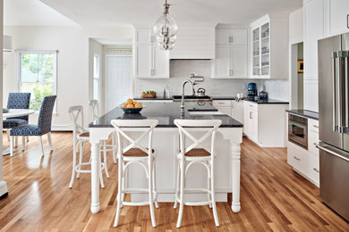 Example of a classic medium tone wood floor and brown floor eat-in kitchen design in Boston with a farmhouse sink, white cabinets, white backsplash, subway tile backsplash, stainless steel appliances, an island and blue countertops