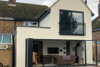 This is an example of a medium sized and beige country two floor rear house exterior in Oxfordshire with a pitched roof, a tiled roof and a black roof.