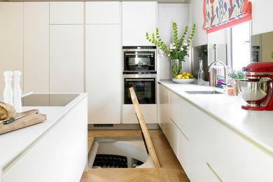 Photo of a mid-sized contemporary l-shaped eat-in kitchen in London with an undermount sink, flat-panel cabinets, white cabinets, panelled appliances, light hardwood floors and with island.