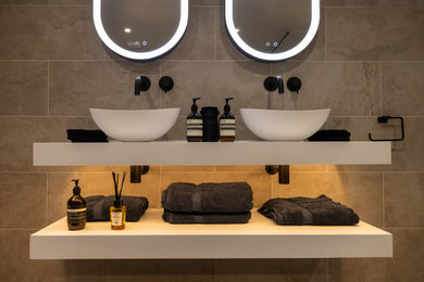 ロンドンにある高級な広いモダンスタイルのおしゃれなマスターバスルーム (白いキャビネット、オープン型シャワー、一体型トイレ	、ベージュのタイル、磁器タイル、磁器タイルの床、コンソール型シンク、ライムストーンの洗面台、オープンシャワー、白い洗面カウンター、洗面台2つ、フローティング洗面台) の写真