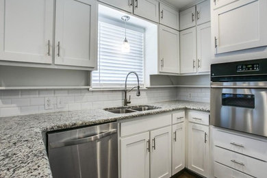 Example of a mid-sized transitional u-shaped dark wood floor and brown floor enclosed kitchen design in Dallas with a double-bowl sink, shaker cabinets, white cabinets, granite countertops, white backsplash, subway tile backsplash, stainless steel appliances, a peninsula and multicolored countertops